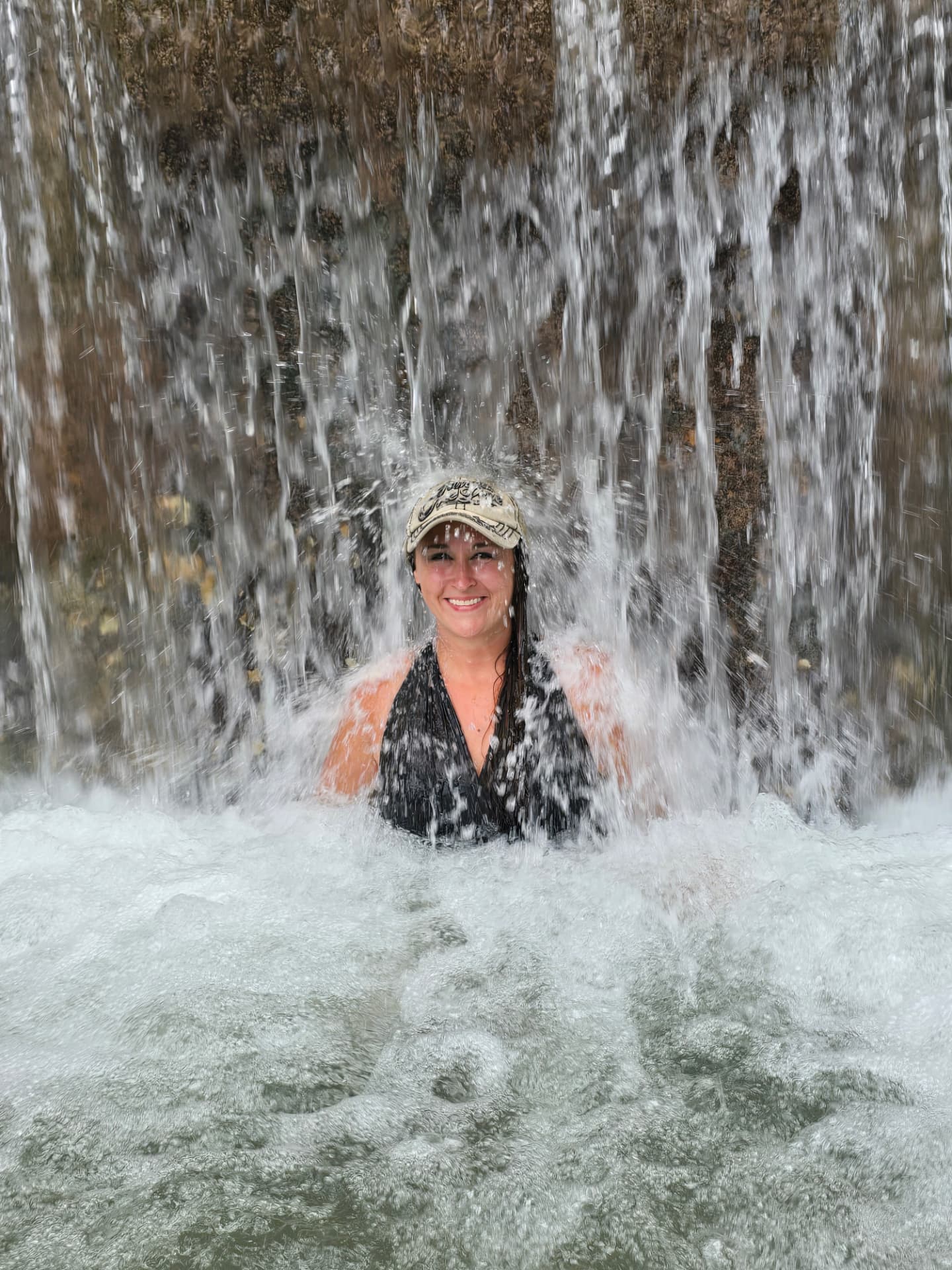 Nikki Bodie smiling in the water directly beneath a rushing curtain of waterfall.