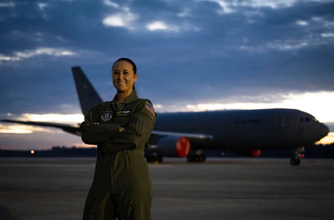 Nikki Bodie in a flight suit standing on the flight line at dusk in front of a tanker aircraft.