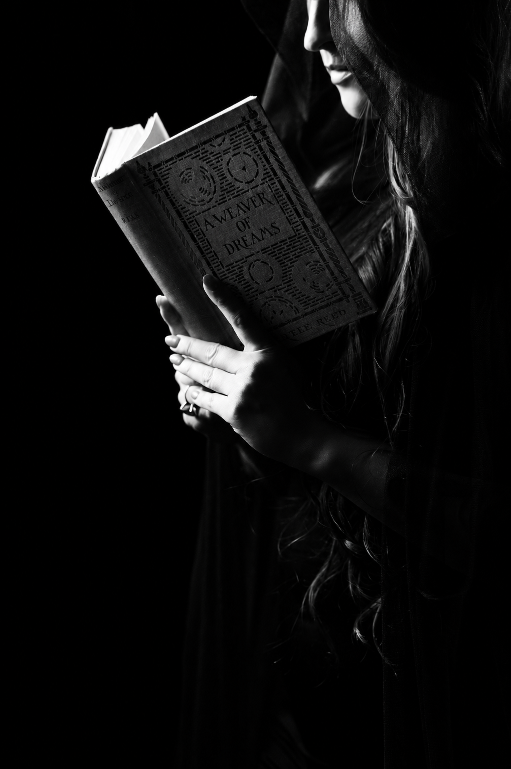 Black and white photograph of hands holding an antique book titled A Weaver of Dreams in near darkness.